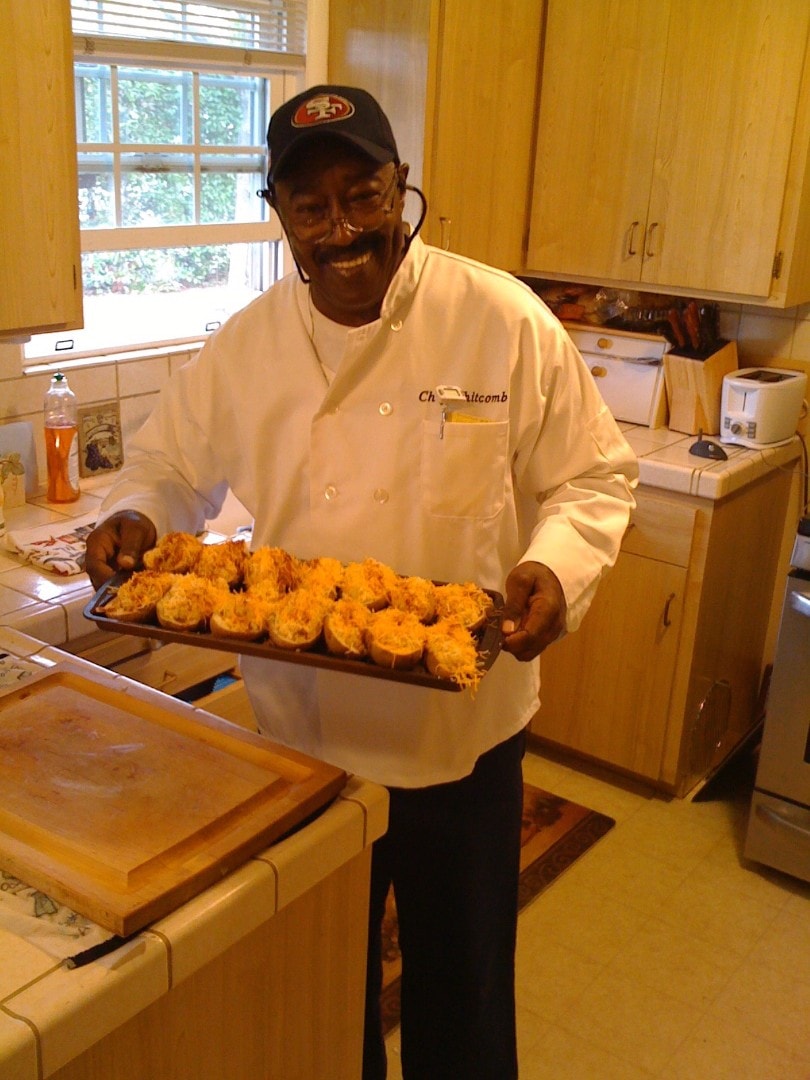 Dr. Charlie Whitcomb in his chef coat, smiling and holding a tray of food he prepared